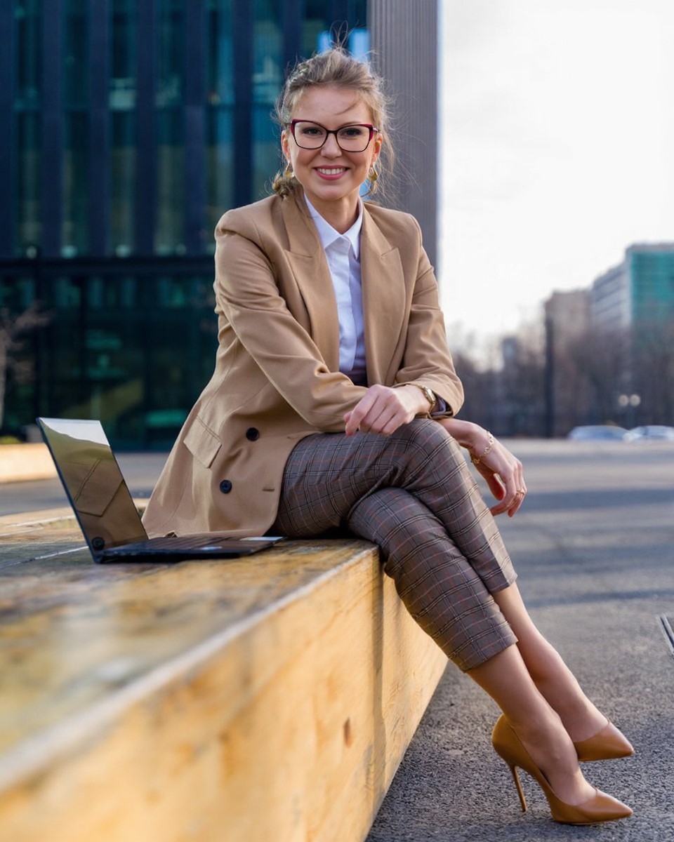 "Lawyer Klimova Anastasia, wearing a beige jacket and glasses, smiles as she sits outside next to her laptop. She specializes in sports law."